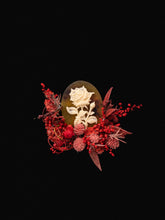 The Rose Birth Flower Ring by CAMELLIA features a detailed white rose on a dark oval, surrounded by red and pink dried flowers. Handcrafted in New York, it offers an adjustable size for a perfect fit.
